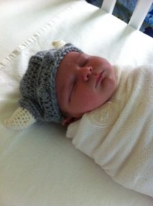 Milo, swaddled up and sleeping, wearing a crocheted viking hat